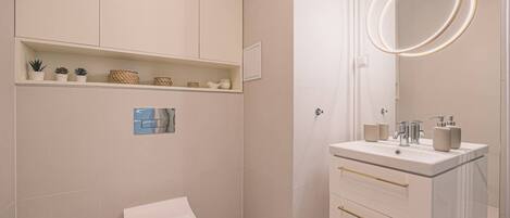 A modern bathroom with a toilet, a vanity with a mirror and lights, and shelves with plants and toiletries.