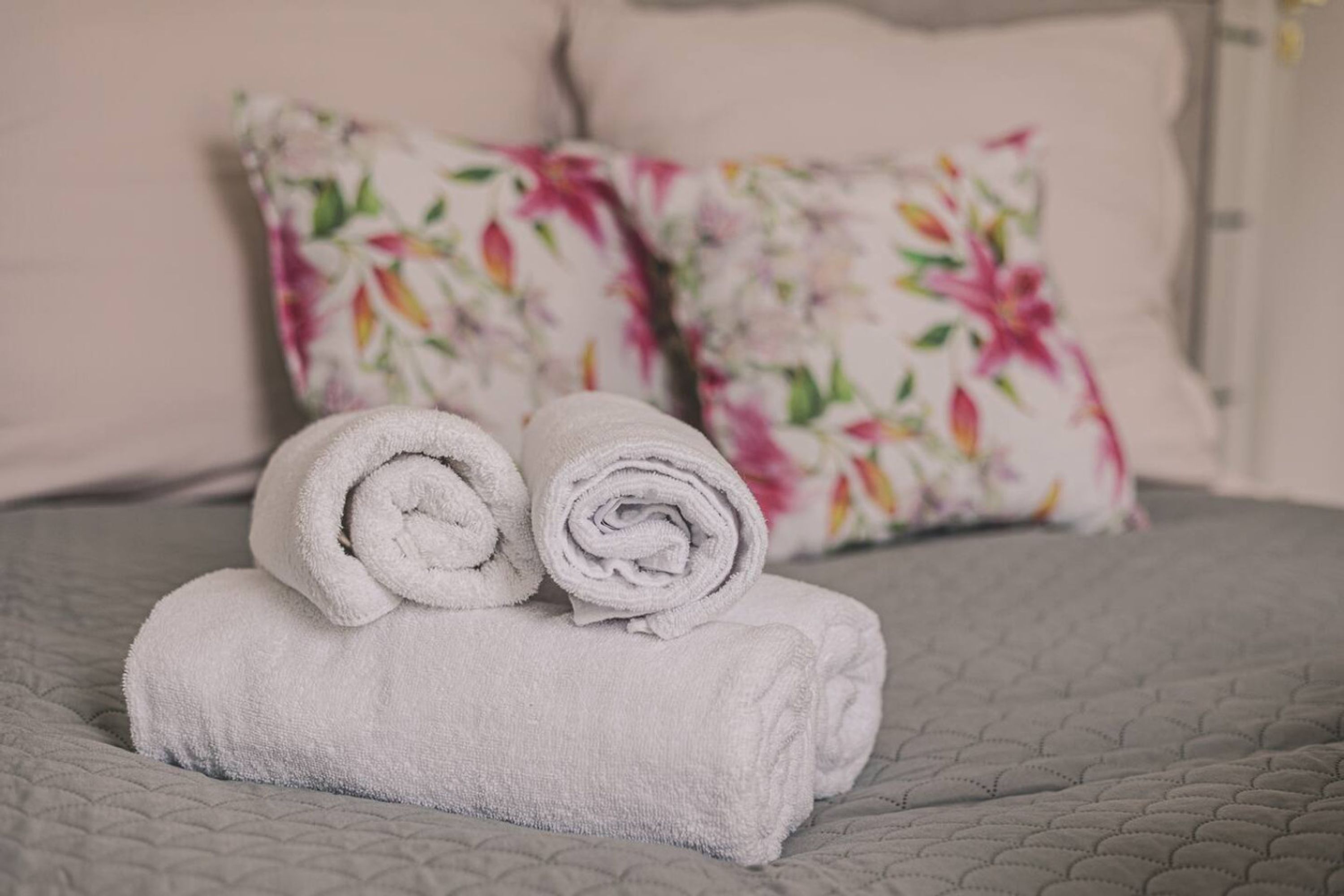A neatly made bed with two rolled white towels and floral-patterned pillows.