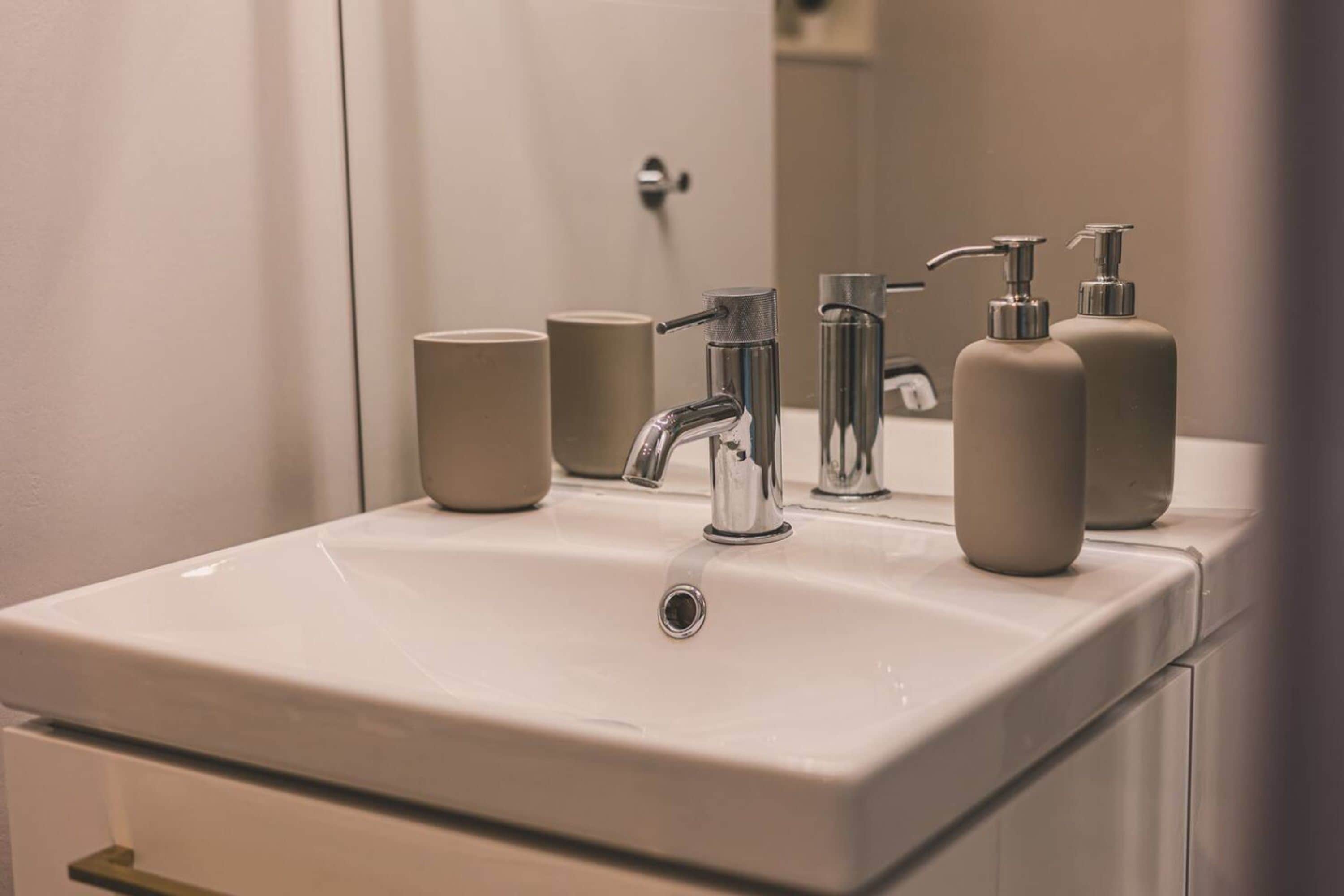 A bathroom with a white sink, a mirror, and two beige bottles on the counter.