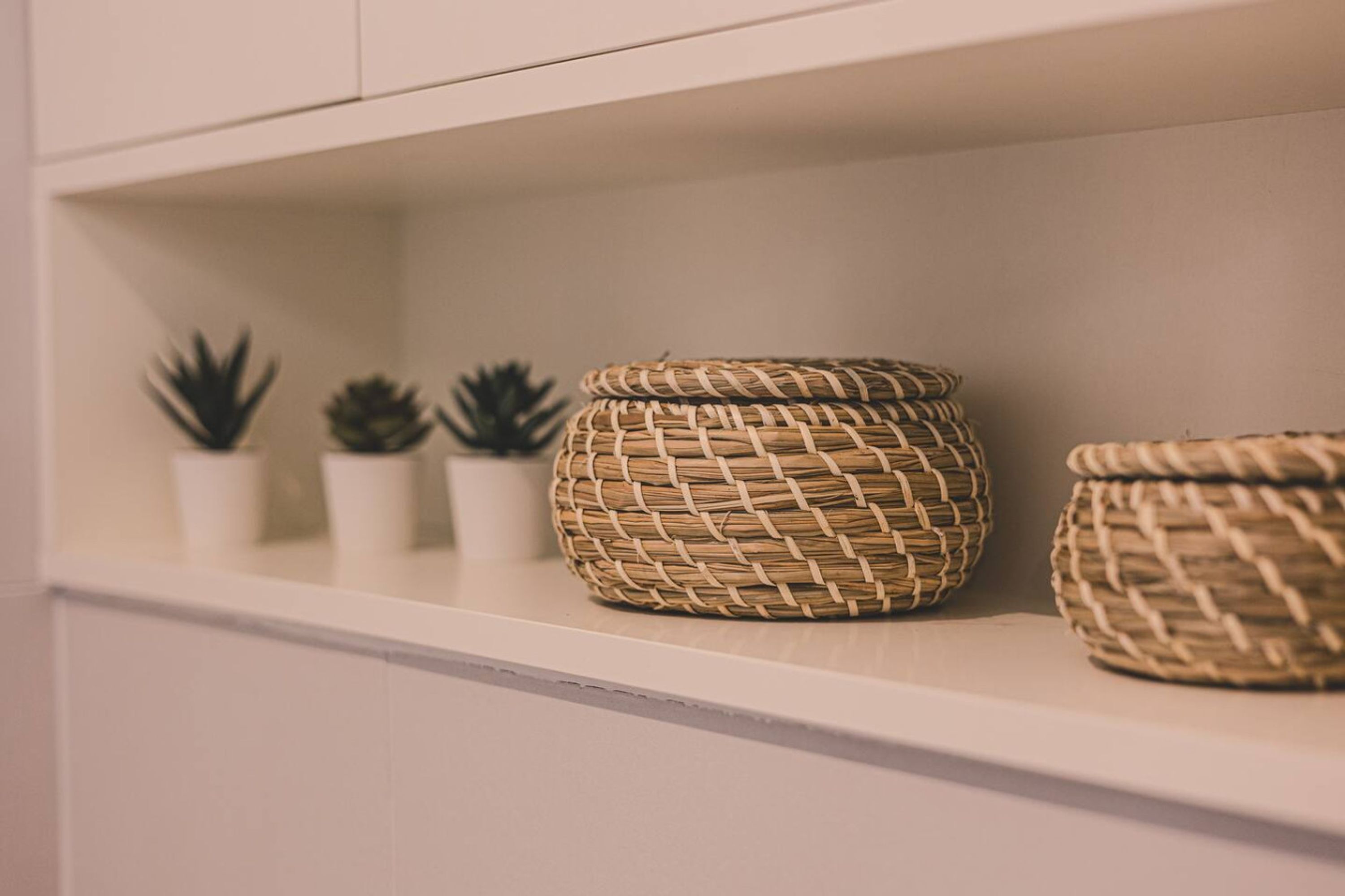 A shelf with woven baskets and small potted plants.