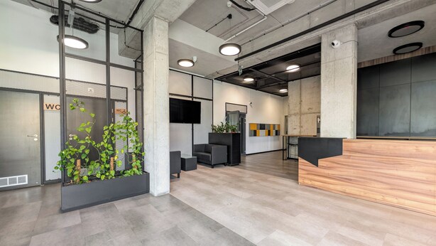 Un espace de bureau moderne comprenant un comptoir d’accueil, un espace détente et un grand écran.