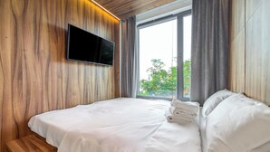 Une chambre moderne avec un mur en bois, un téléviseur à écran plat, une grande fenêtre avec des rideaux et des lits soigneusement faits.