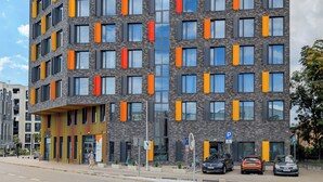 Un bâtiment moderne avec une façade en briques et de nombreuses fenêtres, dont certaines sont dotées de stores orange.
