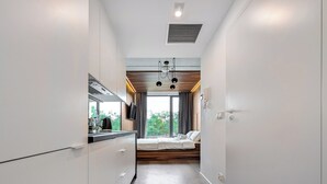 Une chambre d’hôtel moderne dotée d’une kitchenette, d’un lit et d’une grande fenêtre donnant sur un paysage verdoyant.