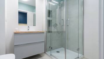 Ein modernes Badezimmer mit einer Glaskabine zur Dusche, einem weißen Waschbecken mit Holzablage und einem Spiegel darüber.