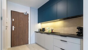 Eine moderne Küche mit Holztür, dunkelblauen Schränken und einer schwarzen Arbeitsplatte, sowie einer Kaffeemaschine.