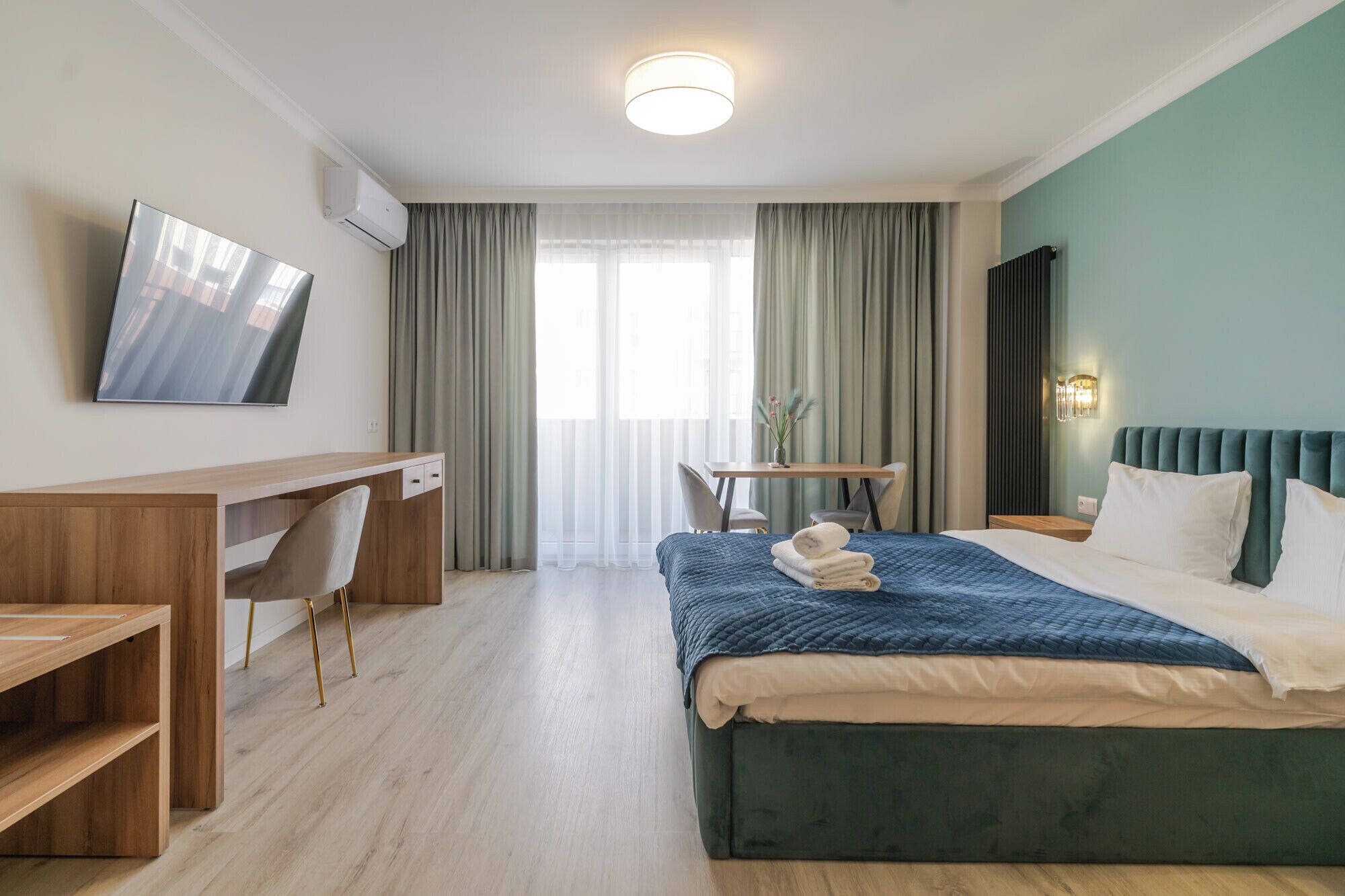 Ein Hotelzimmer mit Bett, Schreibtisch, Stuhl, Fernseher und einem Fenster mit Vorhängen.