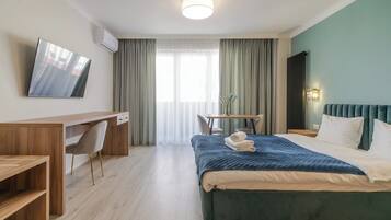 Ein Hotelzimmer mit Bett, Schreibtisch, Stuhl, Fernseher und einem Fenster mit Vorhängen.