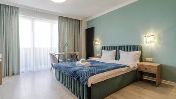 Ein modernes Hotelzimmer mit einem großen Bett, einem Schreibtisch und einem Stuhl. Es gibt ein Fenster mit Vorhängen, eine Wandleuchte und eine Heizung.