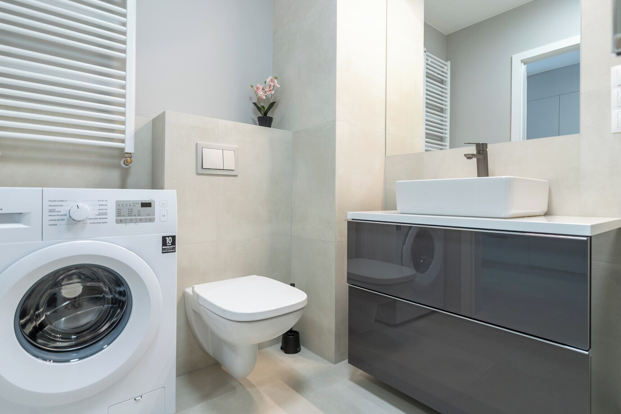 A modern bathroom with a washing machine, toilet, and a large mirror above a sink.