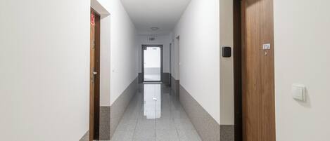 A hallway with a tiled floor, wooden doors, and a light fixture on the ceiling.
