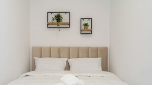 A neatly made bed with white linens and rolled towels, a beige upholstered headboard, and two wall-mounted shelves with potted plants. - Business Deluxe Studio 19 (Katowice)