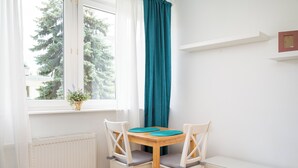 A small dining area with a wooden table and two white chairs, a window with a view of trees, and a teal curtain.