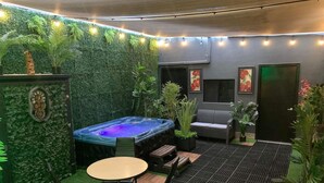 A cozy indoor garden with a hot tub, seating area, and decorative plants.