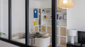 A modern living room with a dining area, white furniture, a wicker lamp, and a television. - 1-Br with Terrace – Palm Beach, Close to Beaches (Cannes)