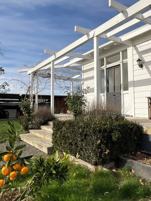 A house with a covered porch, a front door, and a small garden with plants and a tree. - Comfortable family home with rural outlook near village (Havelock North)