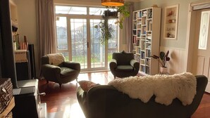 Ett vardagsrum med en soffa, två fåtöljer, en bokhylla och ett stort fönster med gardiner.