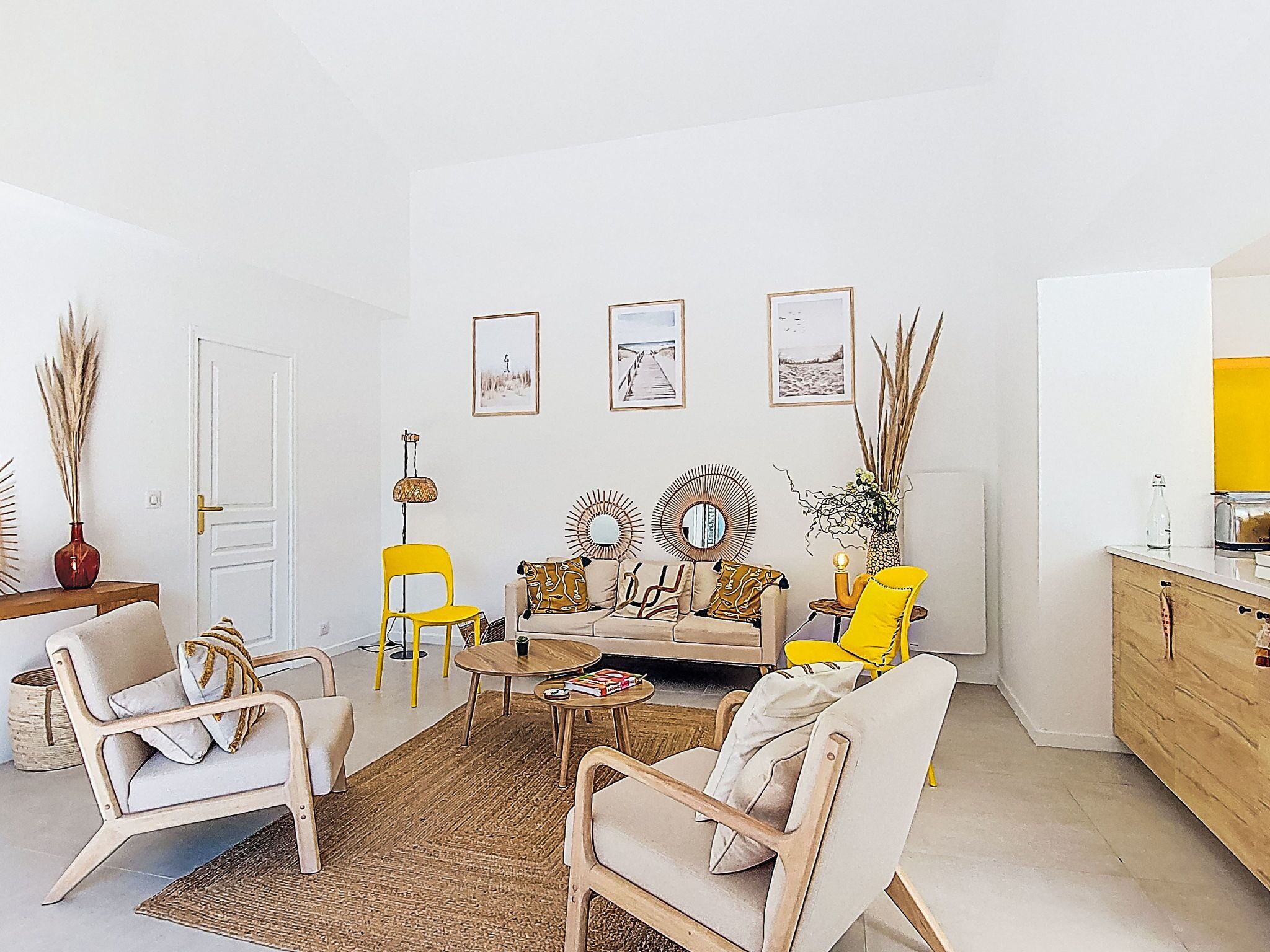 Een woonkamer met een bank, twee fauteuils, een salontafel en een dressoir. Op de muur hangen afbeeldingen in lijsten en op een bijzettafeltje staat een lamp.