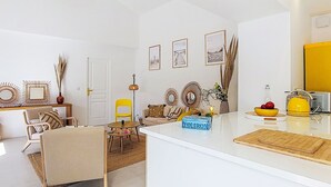 Un salon moderne avec un canapé blanc, un fauteuil jaune et un coin repas agrémenté d’une bouilloire jaune.