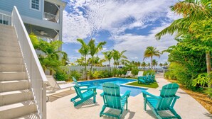A pool area with turquoise Adirondack chairs, a staircase, and a view of a building with balconies.