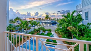 A view of a pool area with lounge chairs, palm trees, and a dock with boats.