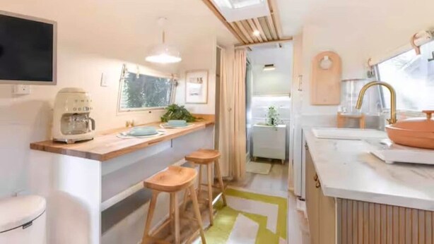 A compact kitchen with a coffee maker, bar stools, a sink, and a window.