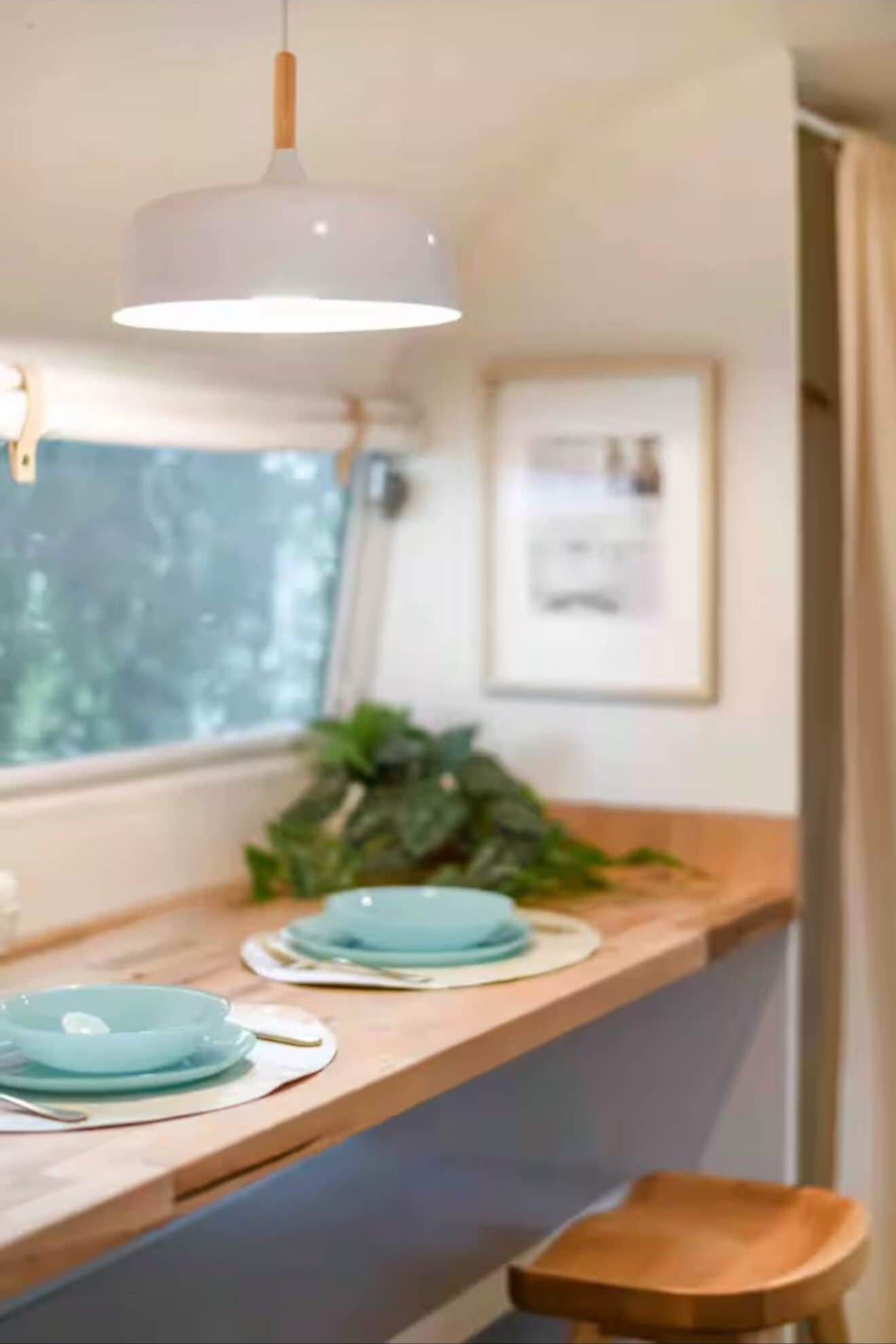 Une cuisine avec une fenêtre, un luminaire suspendu, une plante et un comptoir en bois.