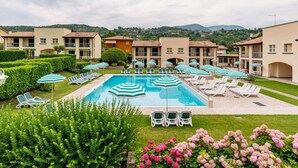 A pool area with lounge chairs and umbrellas, surrounded by neatly trimmed hedges and flowering plants. - Cosy apartment for 4 people with WIFI, A/C, pool, TV and patio (Garda)