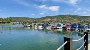 A marina with boats docked, a clear sky, and hills in the background.
