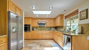 A modern kitchen with wooden cabinets, stainless steel appliances, and a large window providing natural light.
