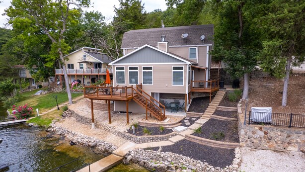 A two-story house with a deck, a small pond, and a stone pathway. - Charming Lake of the Ozarks Cabin, 3BR + Loft, Dock & Fun for All! Sleeps 10 (Rocky Mount)