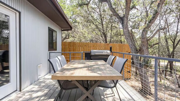 Terraza exterior con mesa y sillas de madera, una parrilla de barbacoa y vistas a árboles.