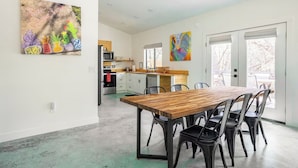 Una cocina moderna con armarios blancos, una mesa de comedor de madera y sillas negras. Hay dos cuadros coloridos en las paredes.