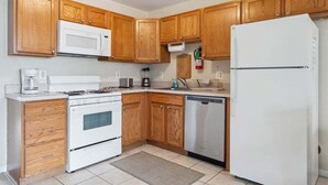 Une cuisine avec des meubles en bois, un micro-ondes blanc, une cuisinière, un lave-vaisselle et un réfrigérateur.