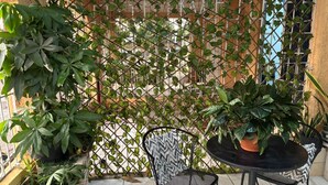 Un petit espace patio extérieur avec une table en métal et deux chaises, entouré de plantes en pot et d’une clôture décorative en métal.