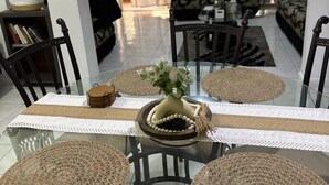 Un coin repas avec une table en verre, des sets de table en fibres tressées et un vase rempli de fleurs.