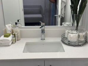 Un baño con un lavamanos blanco, un espejo y varios artículos de aseo en la encimera.