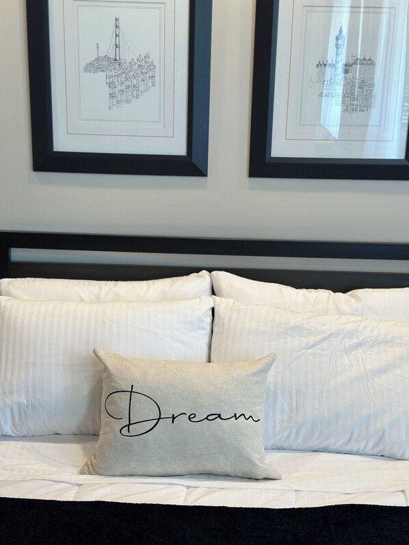 A bed with white bedding and a pillow with the word "Dream" on it. There are two framed pictures on the wall above the bed. - Next Level Living in Niagara! (Niagara Falls)