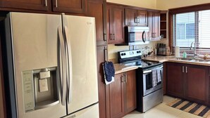 A kitchen with wooden cabinets, a stainless steel refrigerator, a microwave, an oven, and a sink.