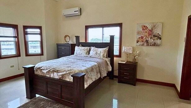 A bedroom with a large bed, a nightstand, a dresser, and a window with blinds.