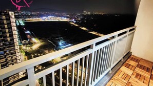 A night view from a balcony overlooking a cityscape with illuminated buildings and a road.