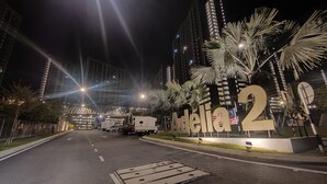 A nighttime street view with illuminated buildings, a large sign reading "Adelia 2", and a road with a manhole cover in the center.