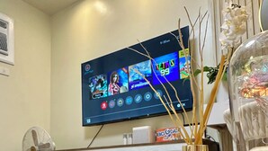 Eine Nintendo Switch Konsole steht auf einem Tisch, im Hintergrund ist ein Fernseher mit einem Spiel zu sehen.