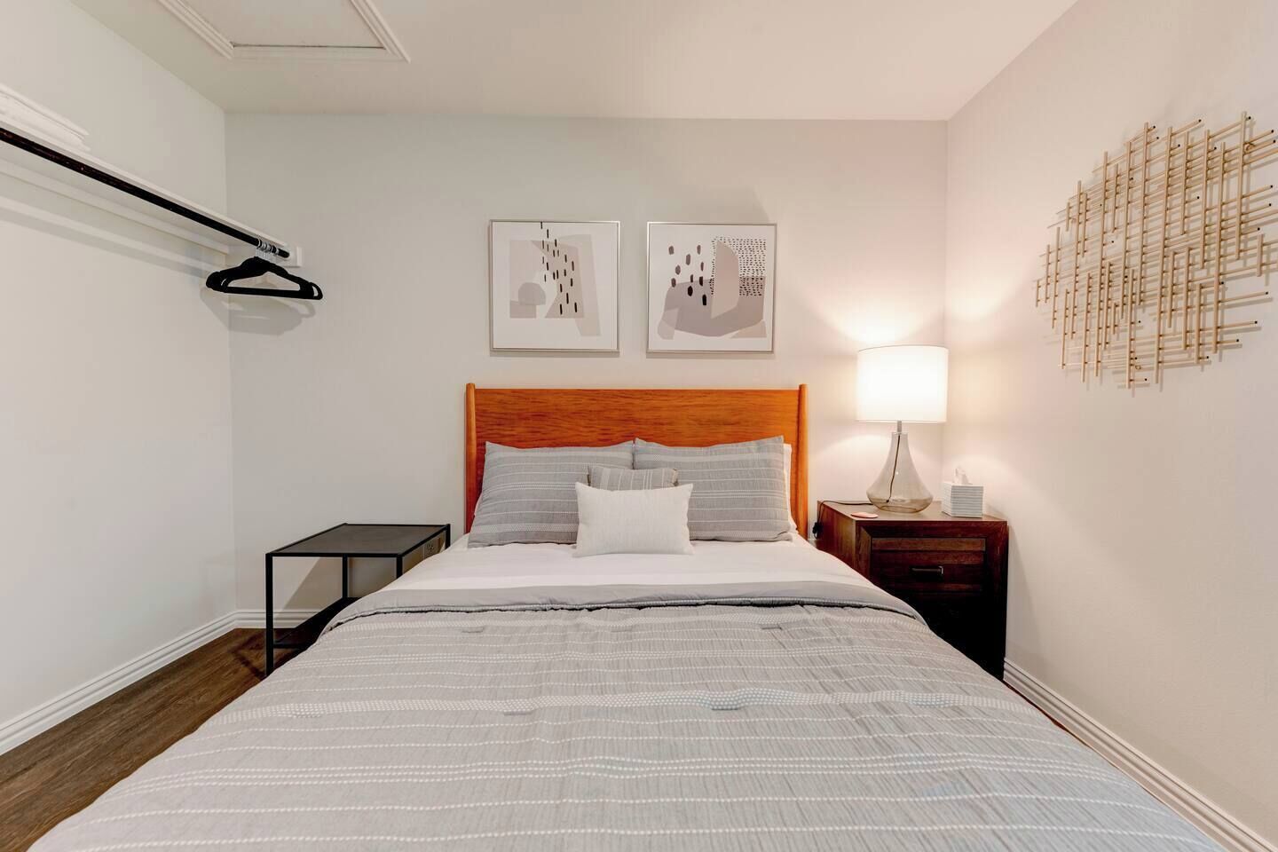 A hotel room with a bed, a nightstand, a wall-mounted lamp, and two framed artworks.