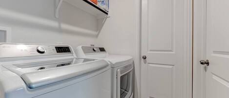 A laundry room with two front-loading washers and dryers, a shelf above the dryers, and a white door.