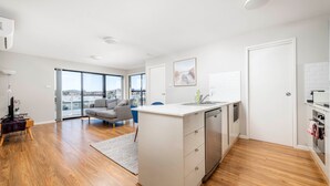A modern apartment with a kitchen, dining area, and a balcony with a city view. - The Greenway Edit Canberra, ACT (Greenway)