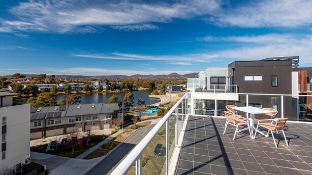 A residential area with modern buildings, a view of a lake, and a balcony with outdoor furniture. - The Greenway Edit Canberra, ACT (Greenway)
