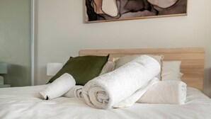 A neatly made bed with rolled white towels, a wooden headboard, and a green pillow. - The Greenway Edit Canberra, ACT (Greenway)
