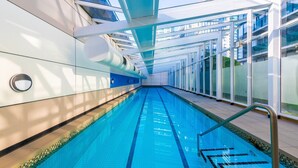 A modern indoor swimming pool with clear glass walls, a tiled floor, and a metal handrail.