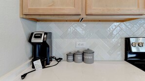 Una cocina con armarios de madera, una cafetera y tres recipientes etiquetados con azúcar, té y café.